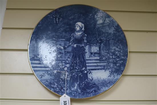 A blue-glazed circular ceramic wall plaque depicting a medieval lady in a garden, Dia 16in approx